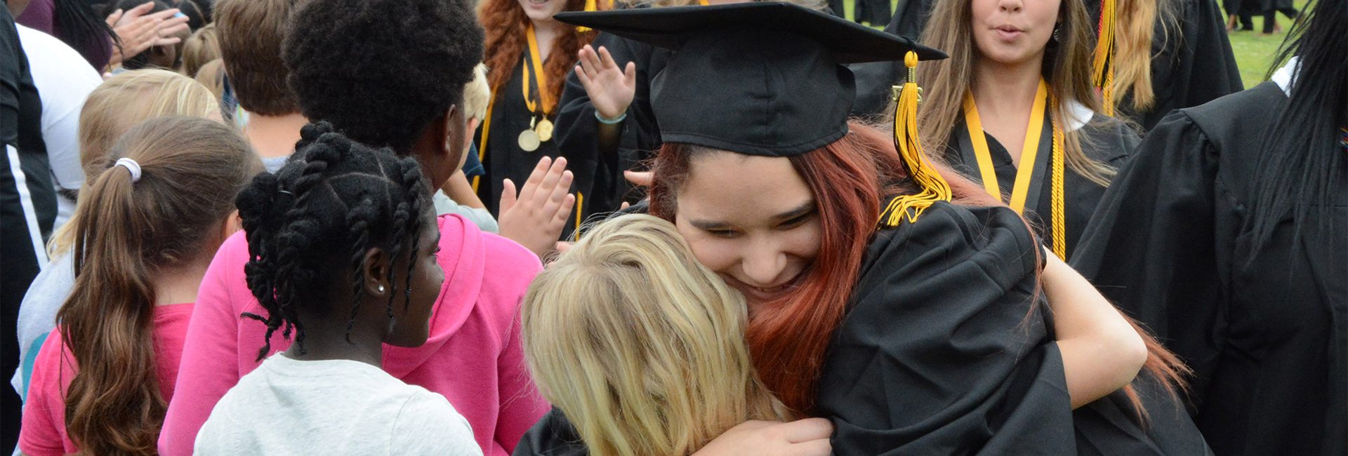 A woman in graduation cap and gown hugging another person.