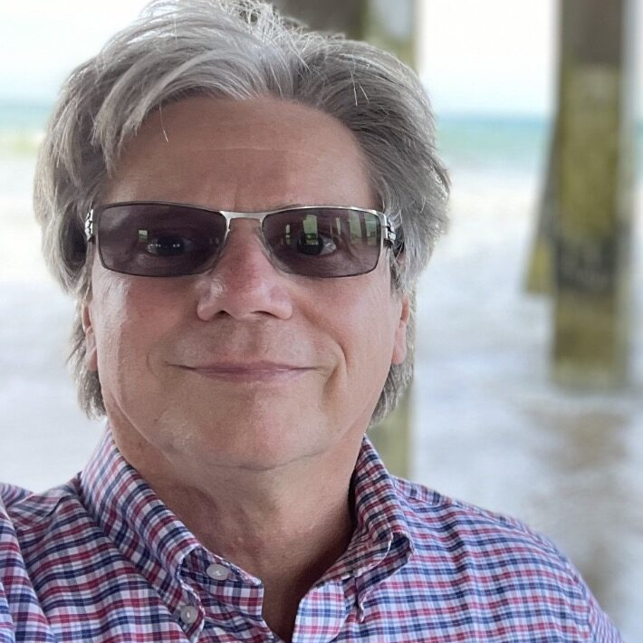 A man with sunglasses on and wearing a plaid shirt.